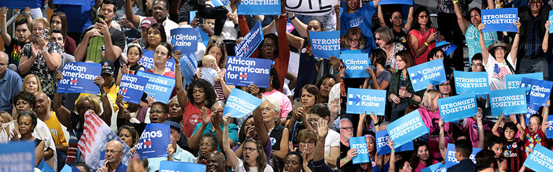 Photo from a Hillary Clinton rally where people are holding up posters that say "Clinton Kaine" and "African Americans for H"