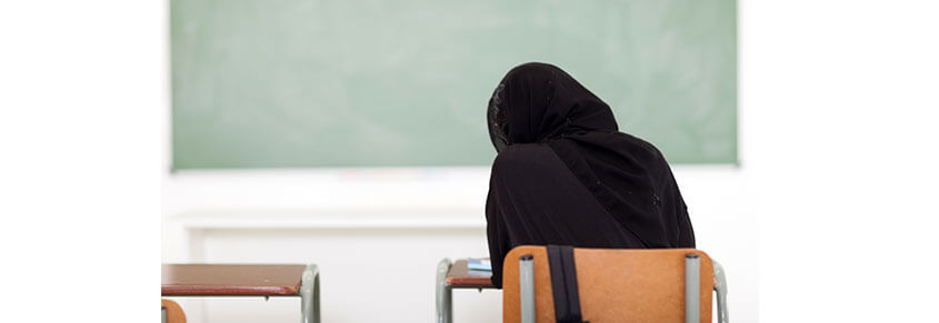 A photo of a kid in a Black sweatshirt sitting in a classroom, facing the board.
