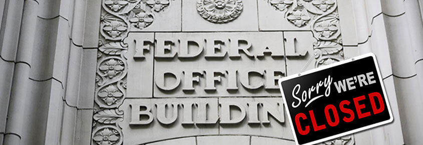 A photo of a Federal Office Building with a "Sorry, we're closed" sign on it.