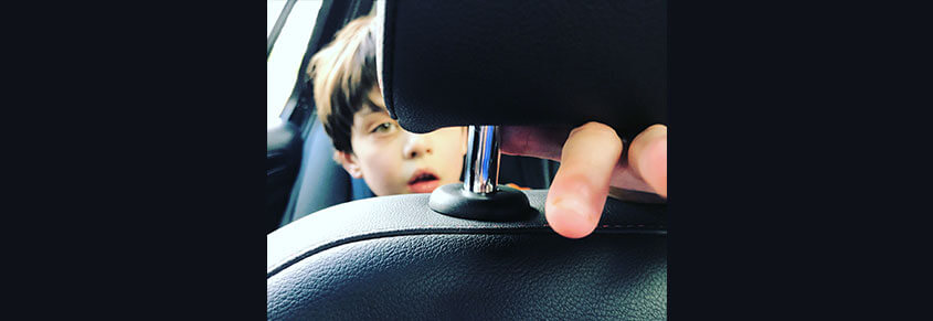 A photo of a young white boy in the back of a car.