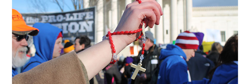 A photo from a pro-life protest. A woman holding Catholic beads is in the center.