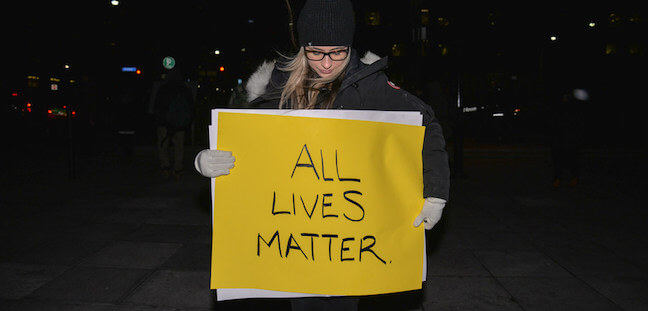 A photo of a white woman holding an "all lives matter" sign
