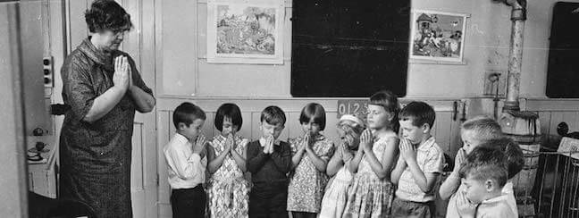 A photo of a teacher praying with her young students.
