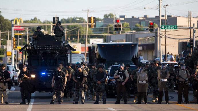 Police officers keep watch while demonstrators protest the death of black teenager Michael Brown in Ferguson