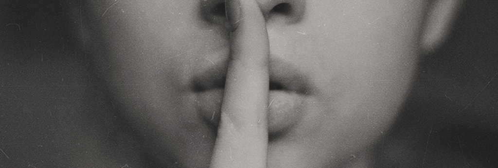 A photo of a woman with a finger of her lips making a shush sign.