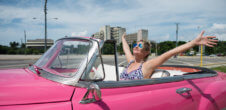 A photo of a woman putting her hands in the air in a pink car