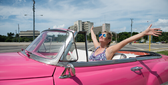 A photo of a woman putting her hands in the air in a pink car