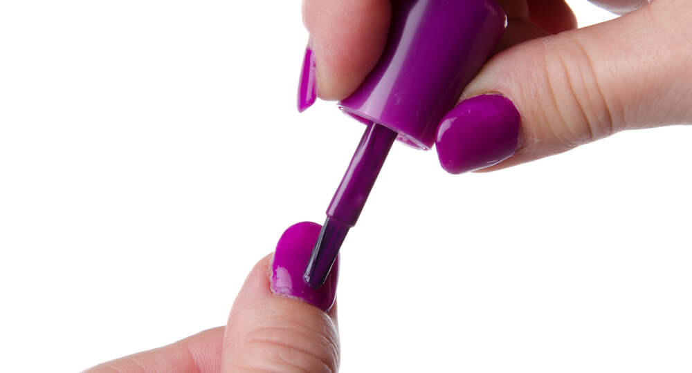 A photo of someone painting their nails purple.