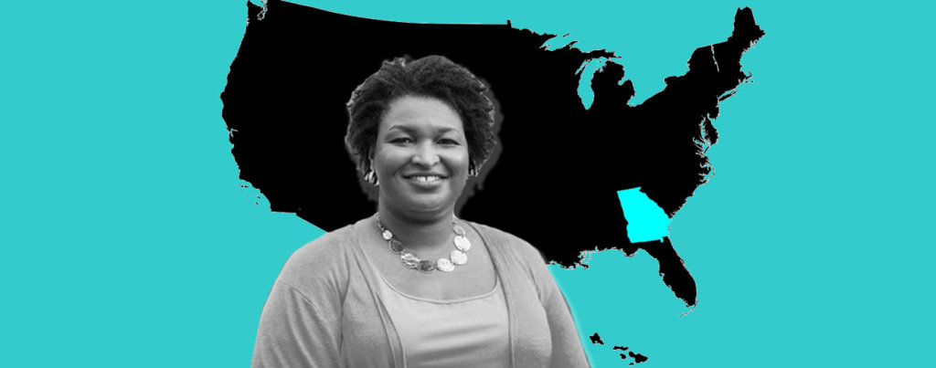 A photo of Stacey Abrams in front of a map of the United States which is black, except the state of Georgia is blue.
