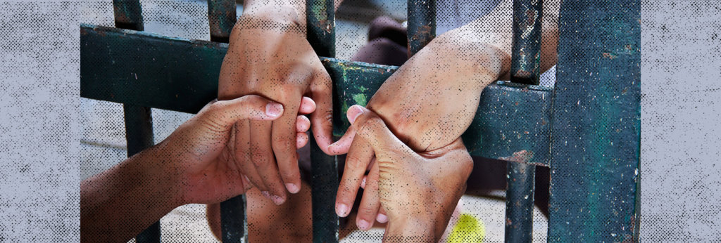 A photo of someone holding someone else's hands. Jail bars are separating them.
