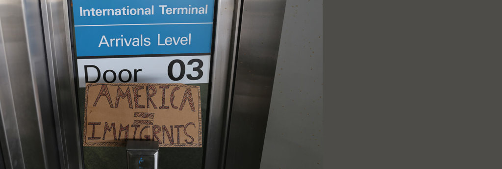 A photo at an airport near an arrivals point. There is a sign that says "America=Immigrants"