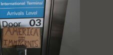 A photo at an airport near an arrivals point. There is a sign that says "America=Immigrants"