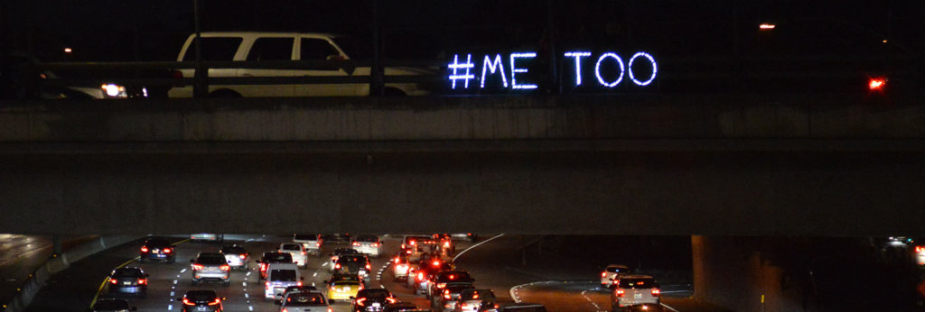 A highway at night with lights on a bridge that Say "#Me Too"