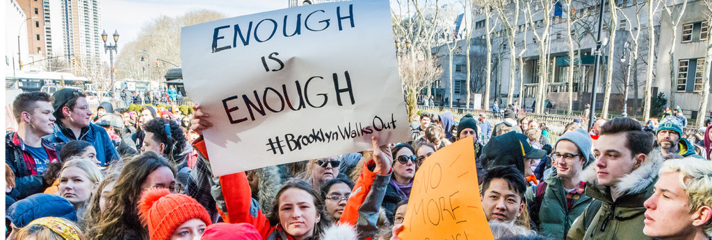 A photo from a protest in Brooklyn. One woman holds a sign that says "Enough Is Enough #BrooklynWalksOut"