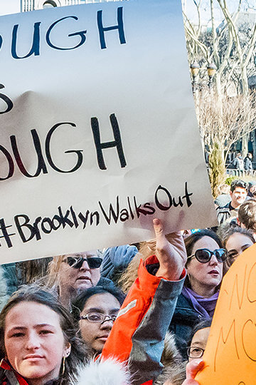 A photo from a protest in Brooklyn. One woman holds a sign that says "Enough Is Enough #BrooklynWalksOut"