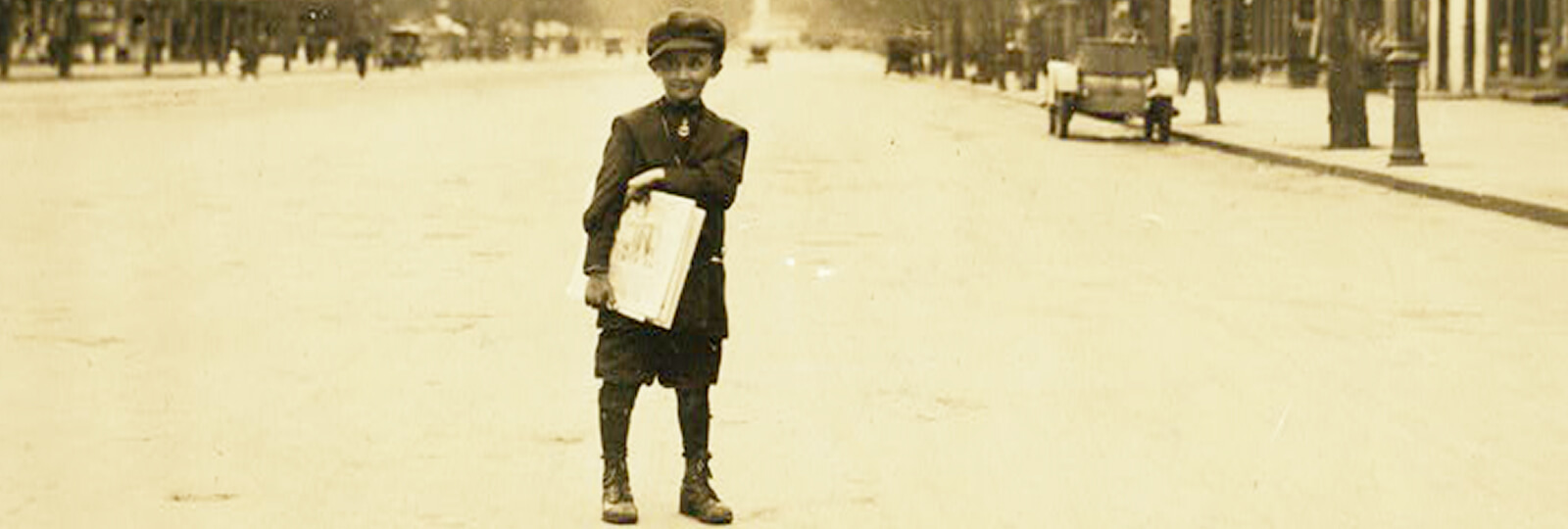 A photo from the early 20th century of a newsboy holding newspapers