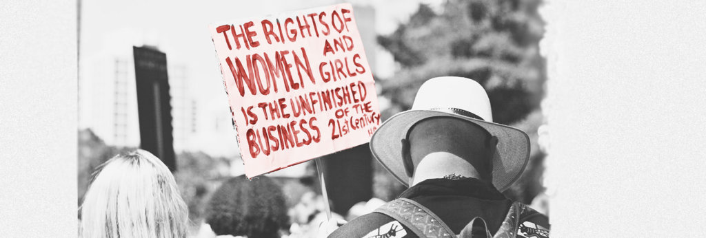 A photo from a protest with a sign that says, "The Rights of Women and Girls is the Unfinished Business of the 21st Century"