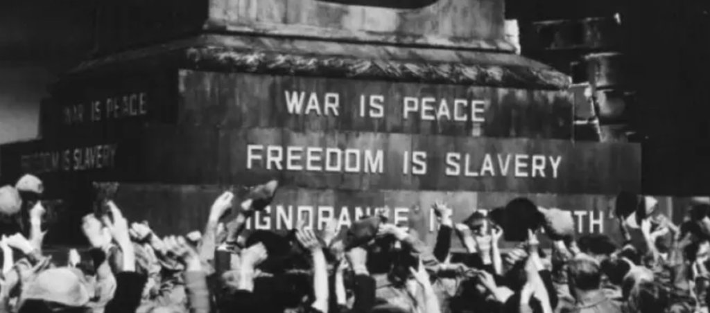 A photo of people in front of a monument that says "War is peace. Freedom is slavery."