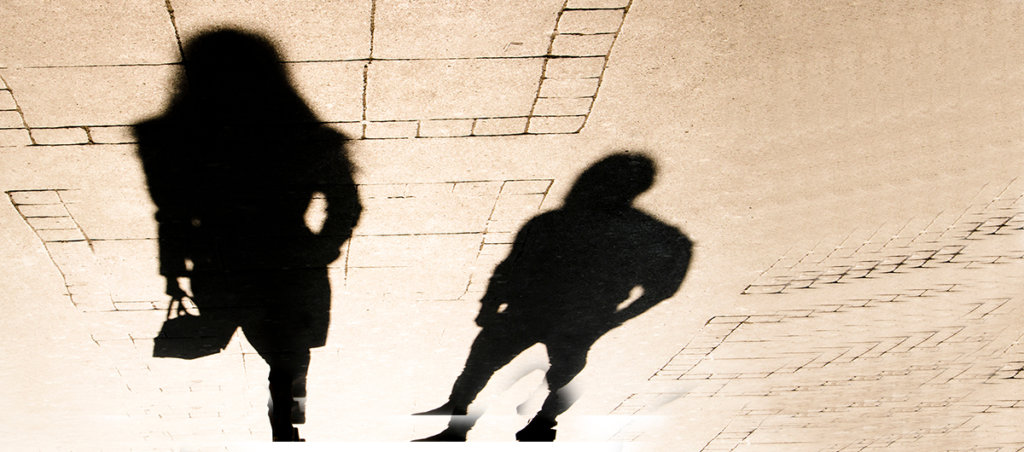 A photo of two shadows. The male shadow seems to be following the shadow of a woman