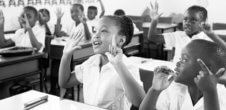 A photo of Black children raising their hands in a classroom.