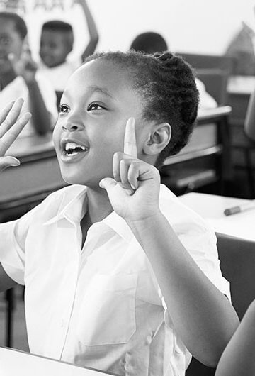 A photo of Black children raising their hands in a classroom.