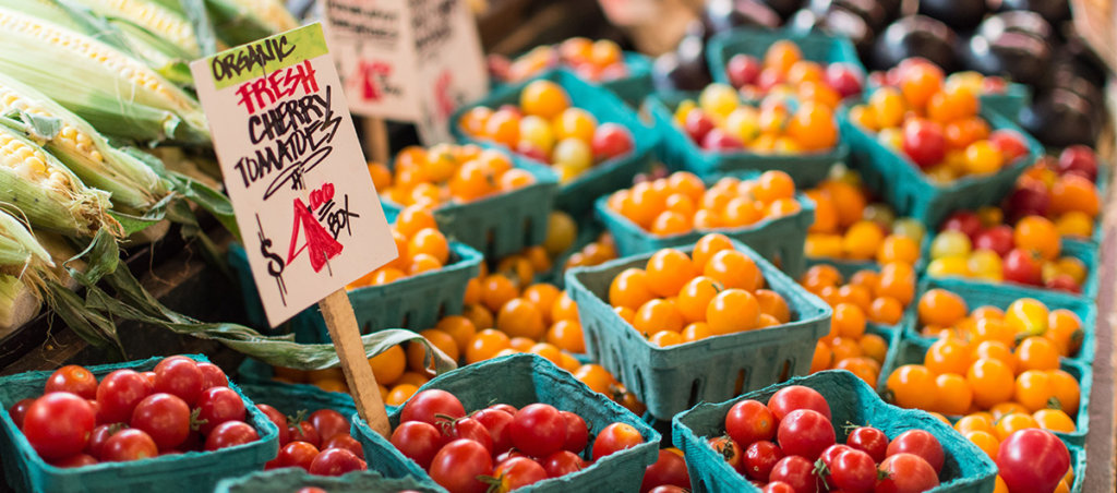 A photo of vegetables including cherry tomatoes and corn, at a farmer's market.