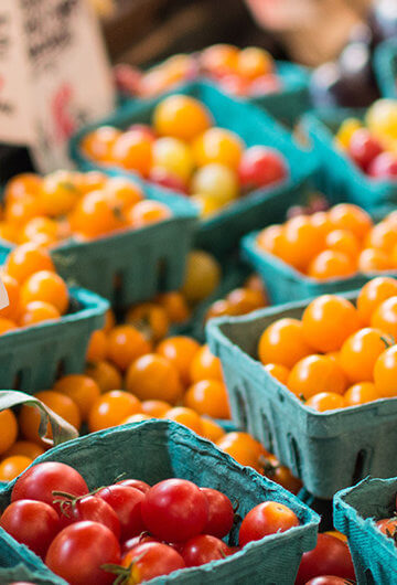 A photo of vegetables including cherry tomatoes and corn, at a farmer's market.