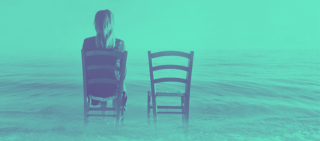 A photo of two chairs in the ocean. A woman is sitting in one of the two chairs.