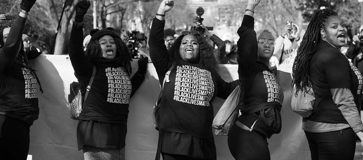 A photo of five Black women at a protest wearing shirts that say "Black Lives Matter" on it.