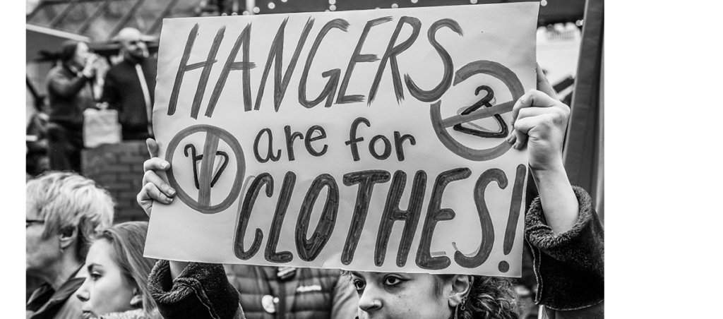 A photo from a protest with a sign that says "Hangers are for Clothes."