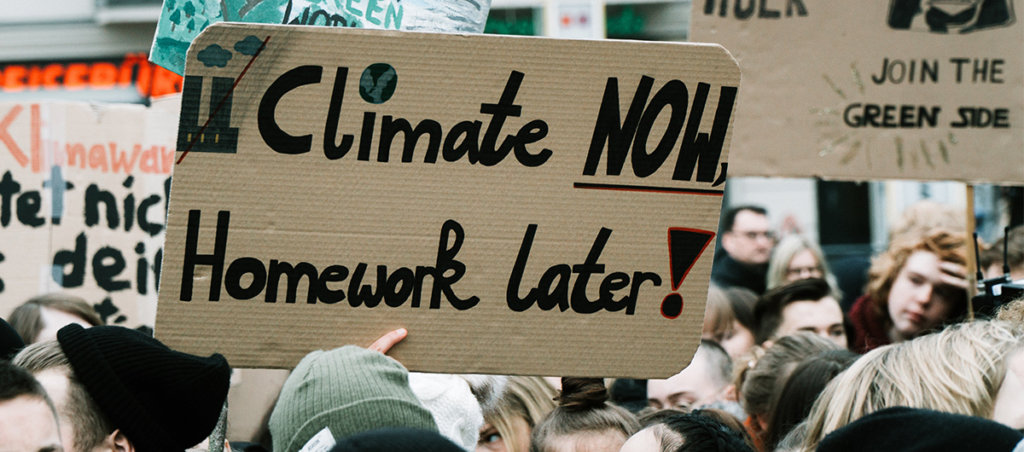 A photo from a climate change protest with the sign, "Climate Now, Homework later" that is visible.