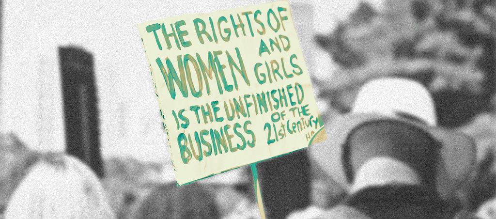 Photo from a protest with the sign "The Rights of Women and Girls Is The Unfinished Business of the 21st Century" is visible.