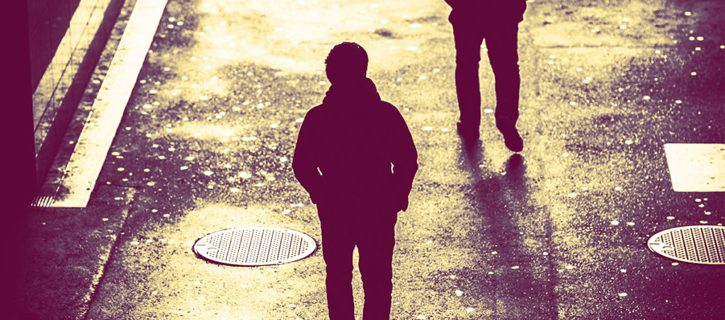 A photo of someone walking on a shadowy area of a city being followed.