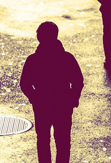 A photo of someone walking on a shadowy area of a city being followed.