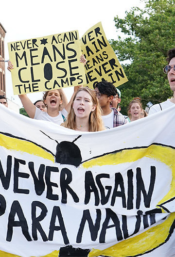 A photo from a protest to close ICE detention centers. People are holding up signs that say "Never Again" and "Never Again Means Close the Camps"