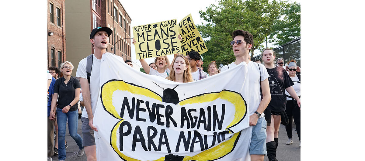 A photo from a protest to close ICE detention centers. People are holding up signs that say "Never Again" and "Never Again Means Close the Camps"