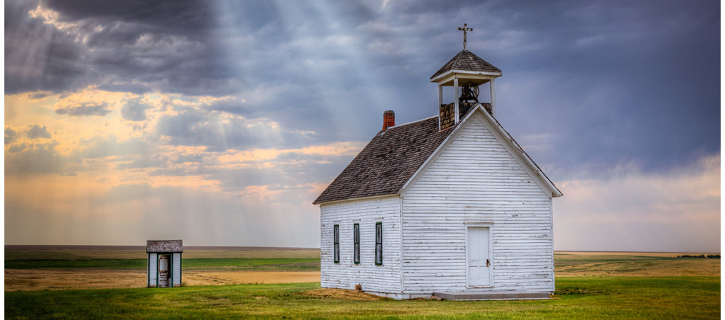 A photo of a small wooden church in a field.