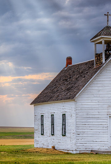 A photo of a small wooden church in a field.