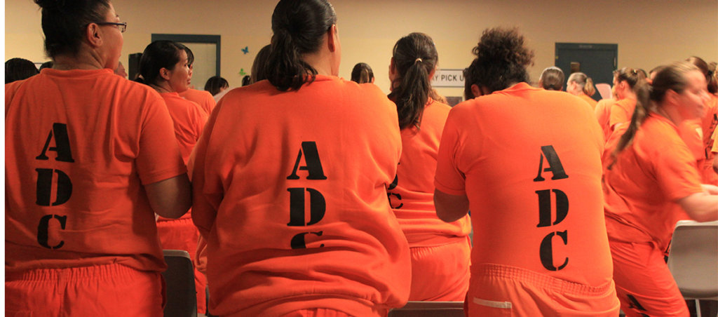 An image of a room of women in prison in orange prison uniforms.