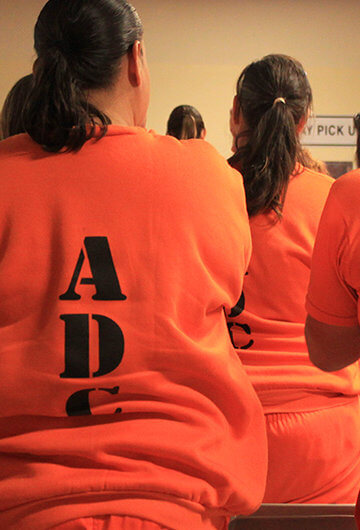 An image of a room of women in prison in orange prison uniforms.