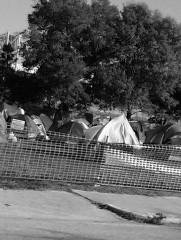 A black and white photo of tents that homeless people live in in a field