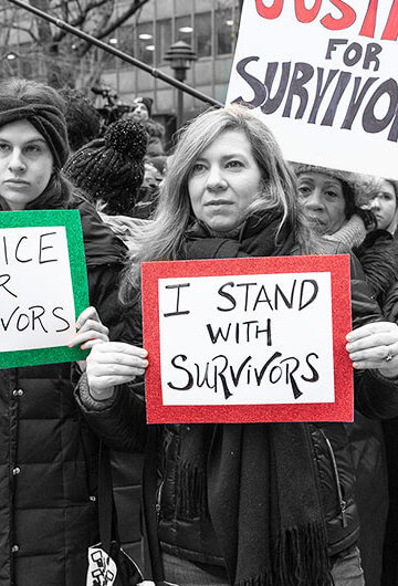 A photo of mainly women at a protest holding signs that say, "Justice for Survivors," "Justice for Survivors," and "Listen to Survivors"