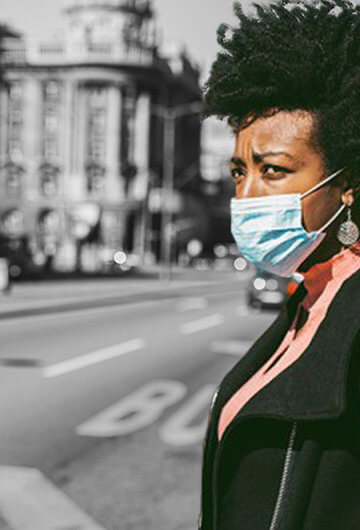 A Black woman wearing a mask on the street of a city