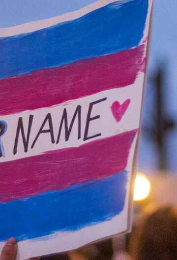 Photo from a protest that says "Say Her Name" with blue and pink on it, which are colors of the trans visibility flag.