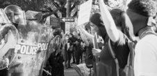 A black and white photos of police in riot gear and protestors holding up signs,