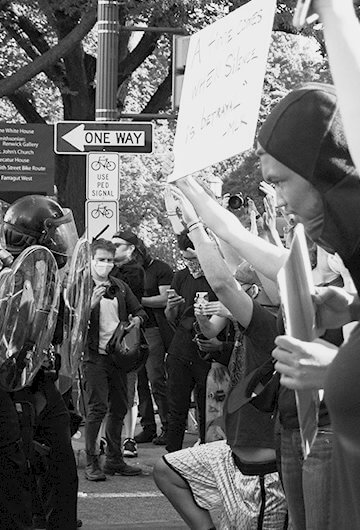 A black and white photos of police in riot gear and protestors holding up signs,