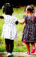 An image of two Black girls in dresses holding hands and walking in the other direction in a grassy area.