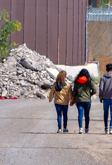 A photo of six people walking to the right and a car to the left.