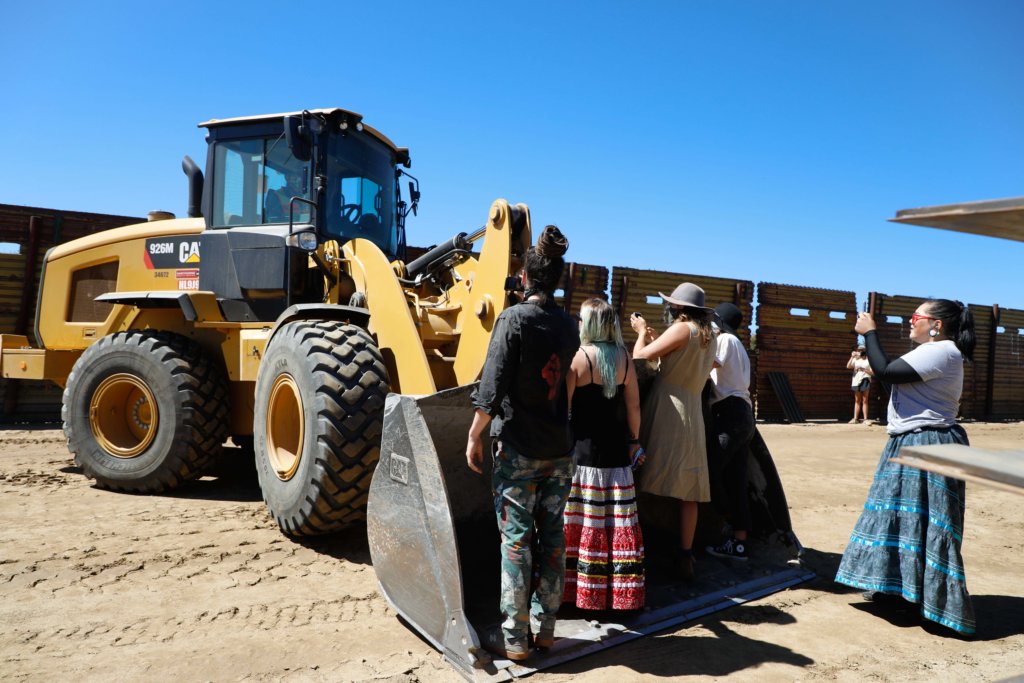 rotestors stand on the bucket of the rear actor to halt the construction of the border wall.
