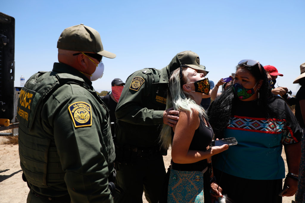A Border Patrol agent places his hand on one of the Kumeyaay woman leaders in the middle of prayer. In Kumeyaay tradition interrupting prayer is a sign of disrespect. The border patrol agent alleges he is trying to keep everyone safe while in a construction zone.